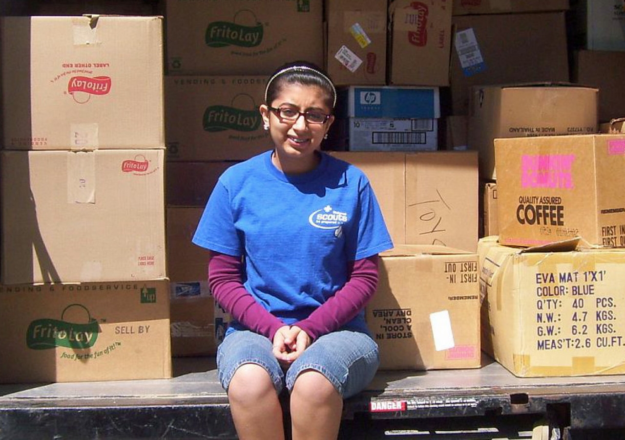 Natasha Tharwani sits among some of the 222 boxes of school supplies collected for donation to RISE International for schools in Angola.