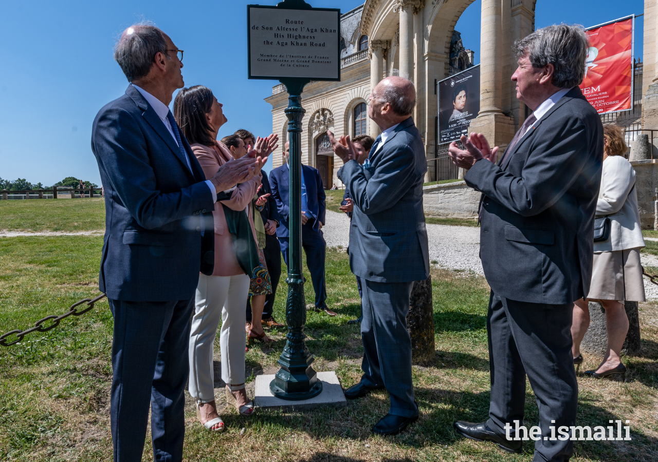 Guests applaud, as a sign for Route Son Altesse l'Aga Khan (His Highness the Aga Khan Road) is unveiled in Chantilly.