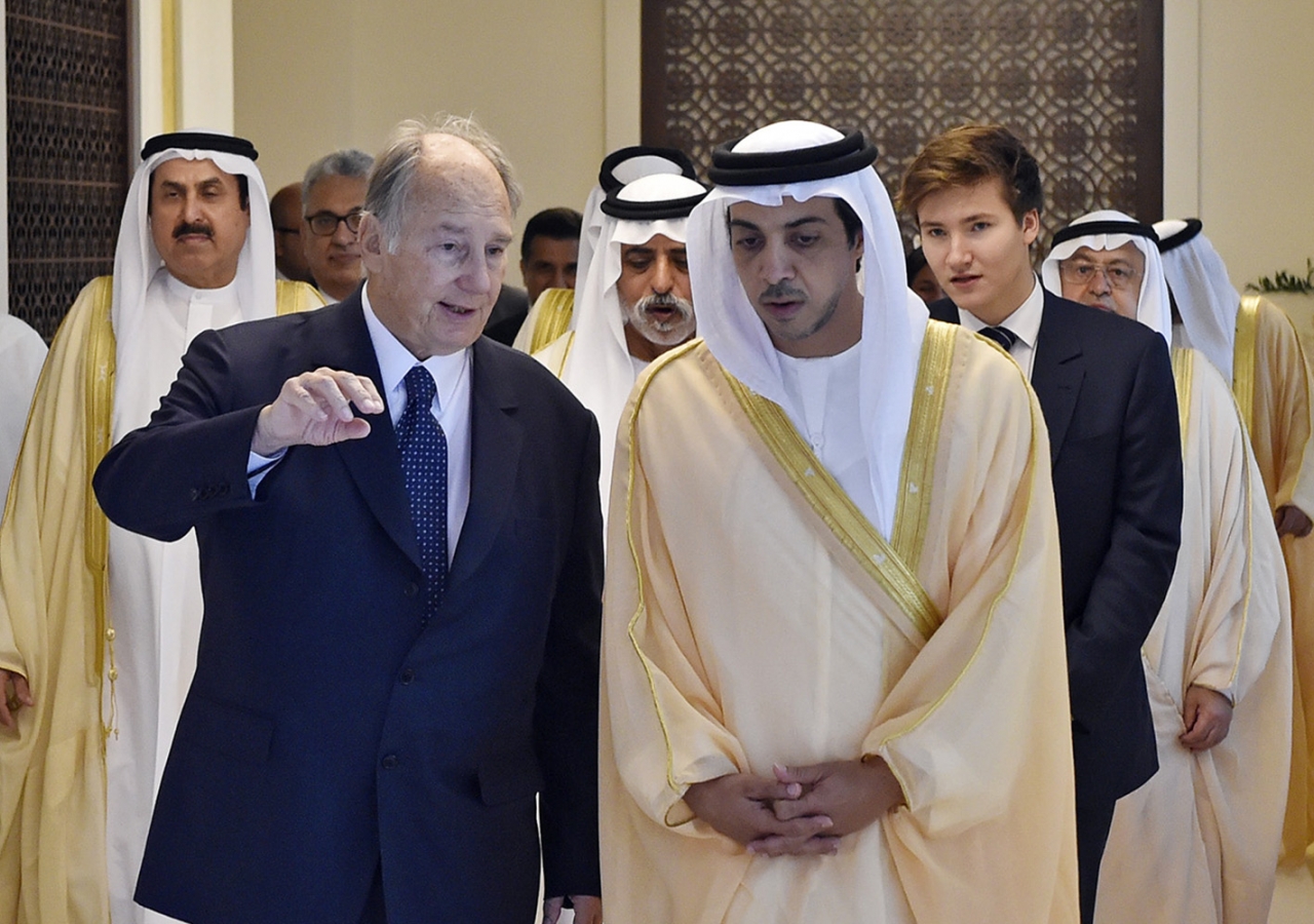 Mawlana Hazar Imam and Sheikh Mansoor engaged in conversation as they walk down a hallway. They are followed by Sheikh Nahyan bin Mubarak Al Nahyan and Prince Aly Muhammad. Gary Otte