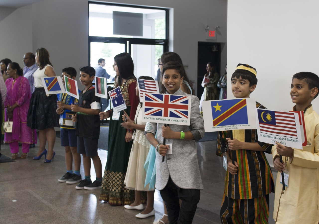 Young children dressed in traditional clothes holding flags from every region where the Ismaili community lives.