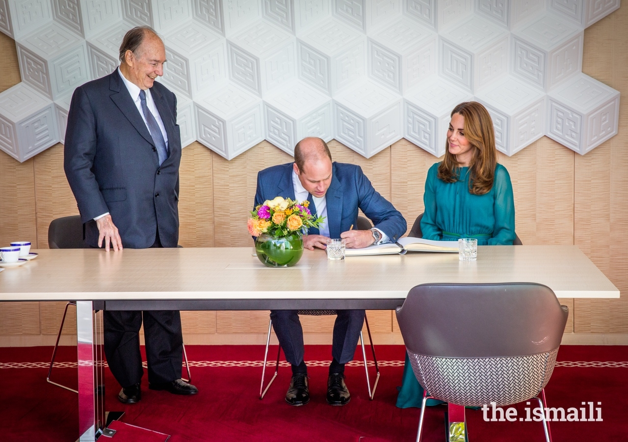 The Duke of Cambridge signs the guest book at the Aga Khan Centre, as Mawlana Hazar Imam and the Duchess of Cambridge look on.