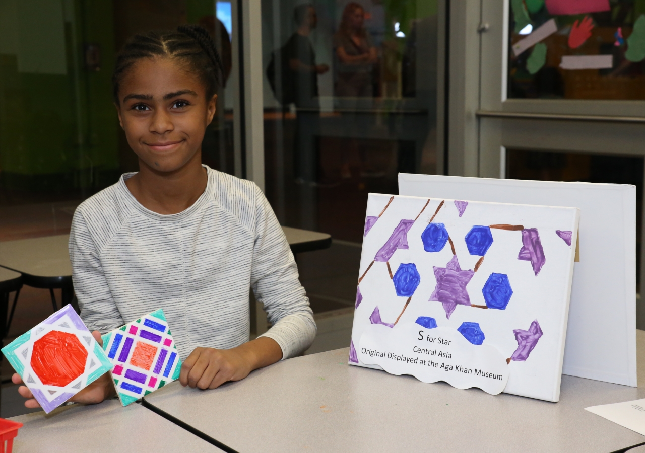A young girl displays her geometric shape tile artwork, featuring traditional elements of Islamic art from the Aga Khan Museum publication, "Astounding ABC."