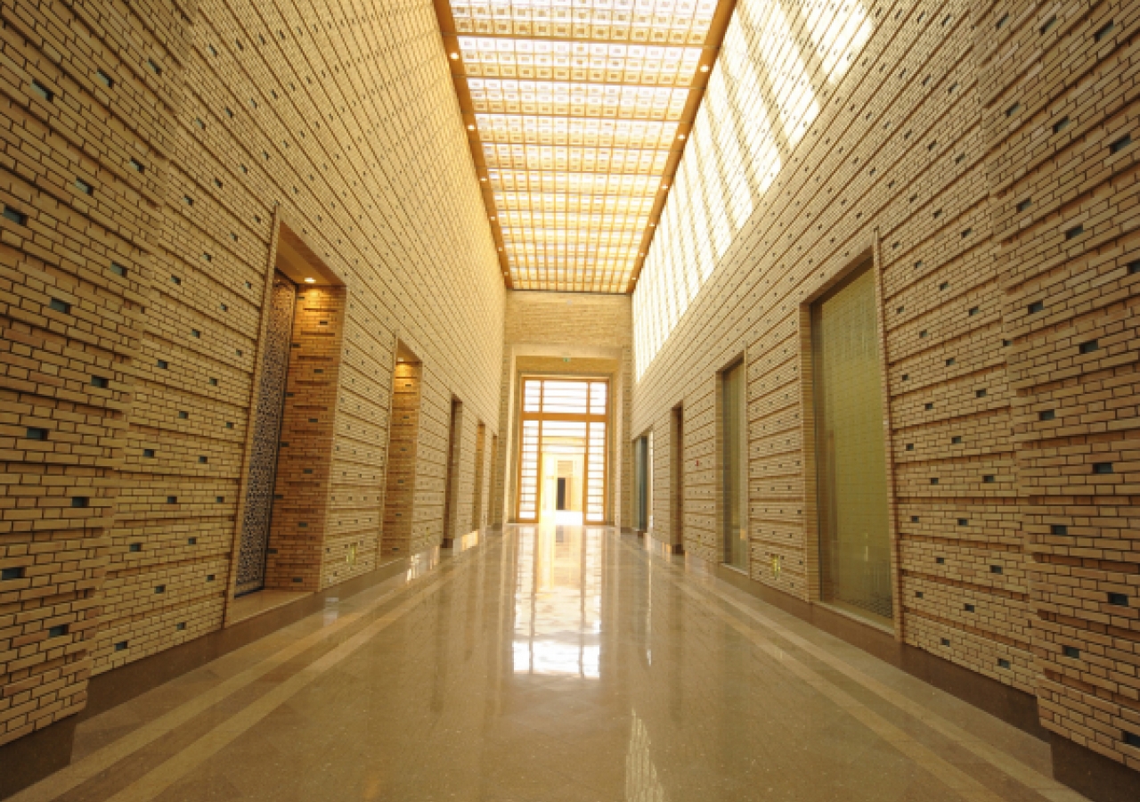 A view down the axial corridor of the administration area from the main entrance of the building. The changing play of light and shade created by sunlight filtering through a wooden lattice, forms patterns on the walls and floor that follow the movement o