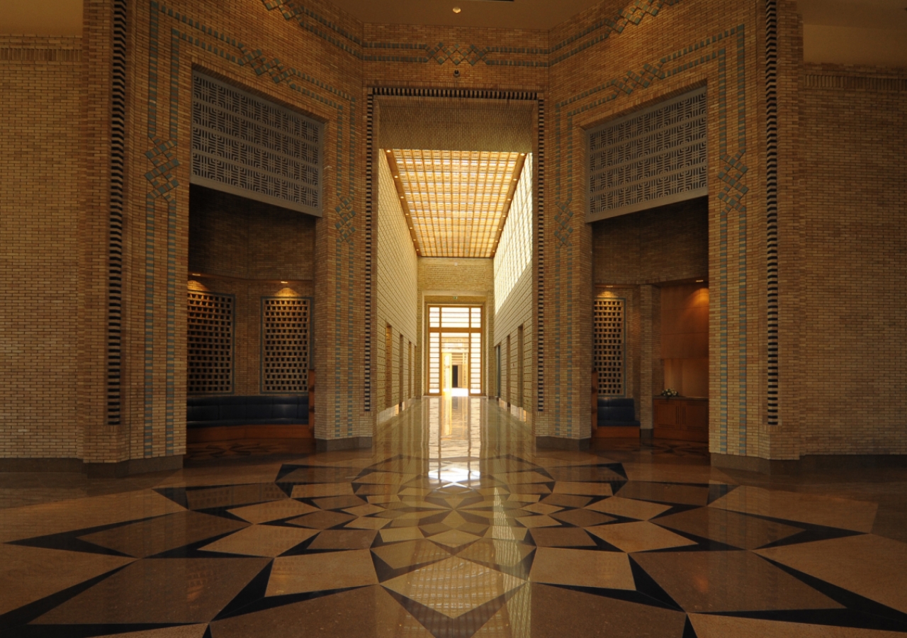 A view from the Main Entrance shows a seating alcove on the left, a reception desk on the right, and the axial corridor of the Administration area leading to the Great Courtyard.