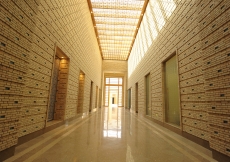 A view down the axial corridor of the administration area from the main entrance of the building. The changing play of light and shade created by sunlight filtering through a wooden lattice, forms patterns on the walls and floor that follow the movement o