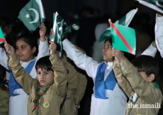 Young scouts and guides waving the national flag, the Ismaili flag and the Diamond Jubilee flag.