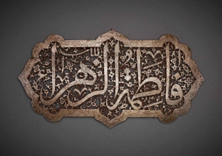 The inscription Fatima al-Zahra’ (“Fatima the Radiant”), the name of the Prophet’s daughter and her epithet, is carved out in an elegant contrast between the solid lines of the magisterial thuluth script and the intricately carved floral spiral that forms its background.